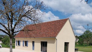 Un edificio a un piano con tetto spiovente, un piccolo portico e un prato.