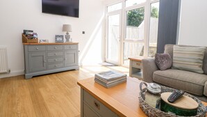 Een woonkamer met een grijze kast, een televisie, een bank en een raam met gordijnen.
