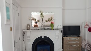 Une pièce avec une cheminée blanche, un miroir au-dessus et un téléviseur posé sur un meuble à droite.