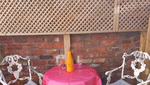 Une table recouverte d’une nappe rose, deux chaises, une bouteille et deux verres, le tout placé devant un mur en briques.