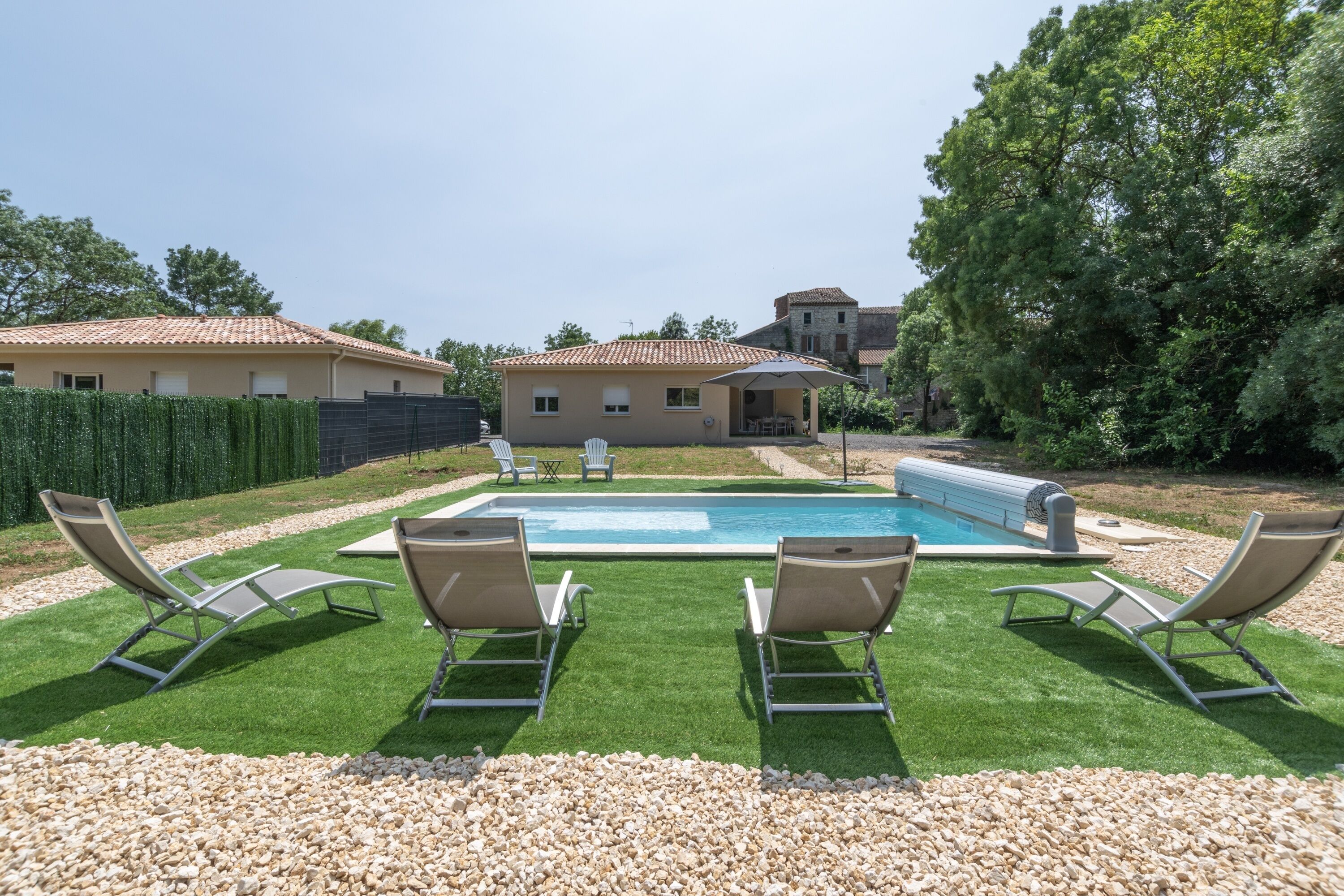A backyard with a swimming pool, four lounge chairs, and a barbecue area.