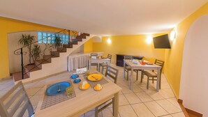 A dining area with a staircase, yellow walls, and a TV mounted on the wall. - B&B La Rosa (Ischia)
