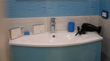 Un bagno con un lavandino bianco, piastrelle blu e un asciugacapelli sul ripiano.