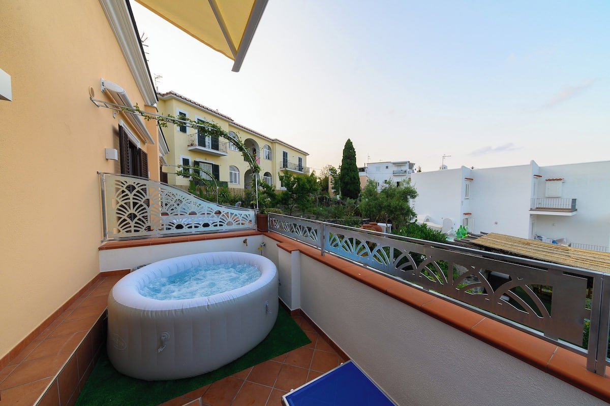 Un balcón con jacuzzi, una baranda decorativa y vistas a edificios cercanos.