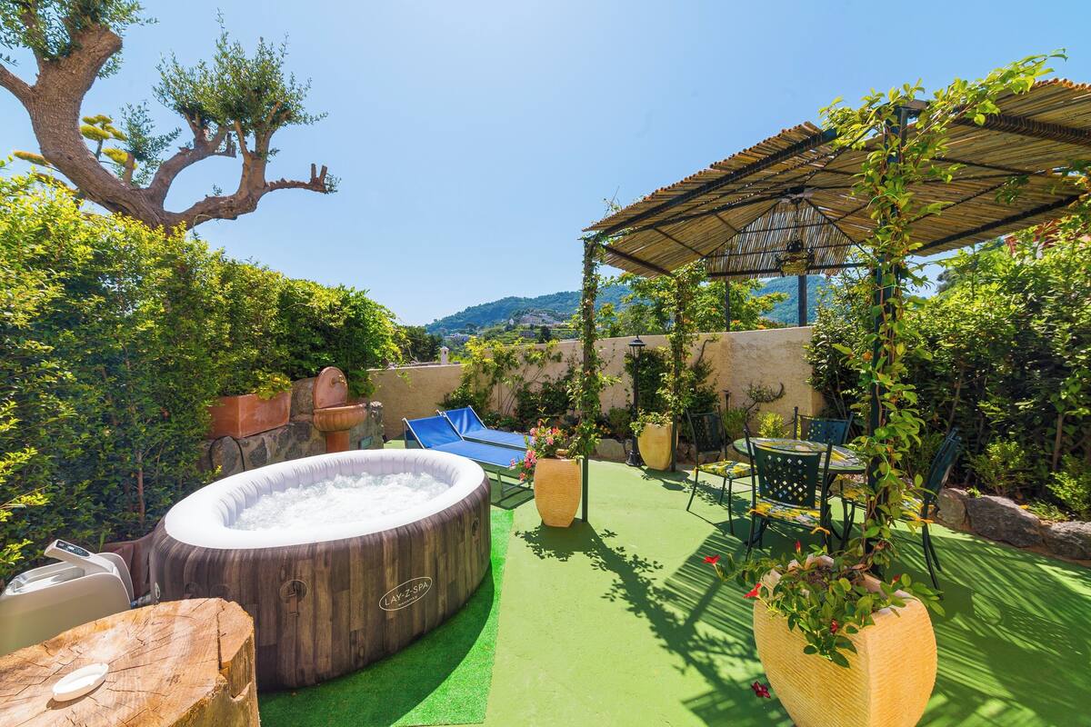 Un jacuzzi, mobiliario de exterior y una pérgola en un exuberante jardín.