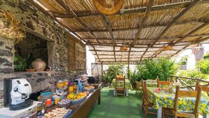 An outdoor dining area with a stone wall, wooden furniture, and a variety of food and drink items. - B&B La Rosa (Ischia)