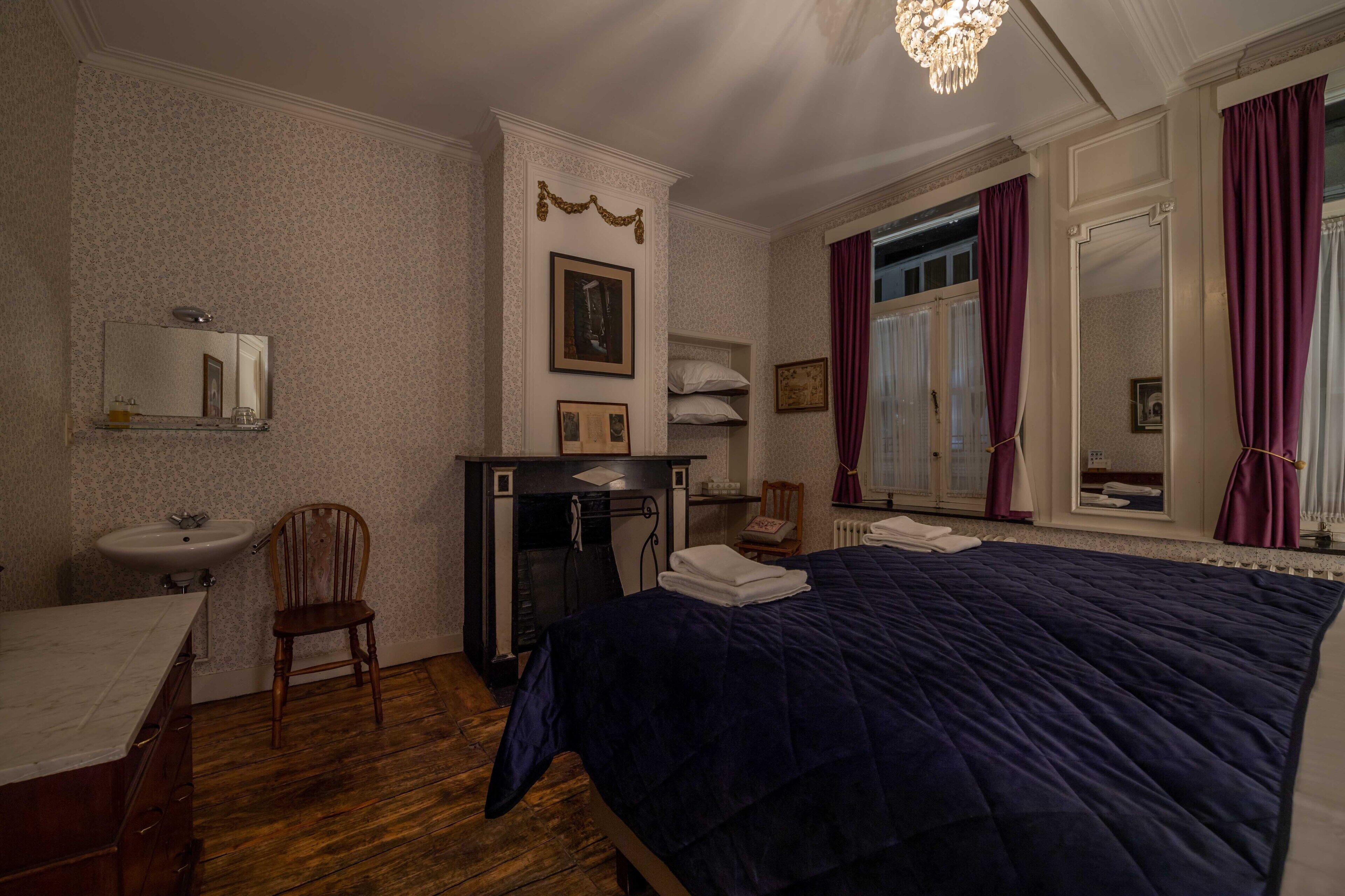 Een slaapkamer met een groot bed, een houten stoel, een dressoir, een spiegel en een open haard.