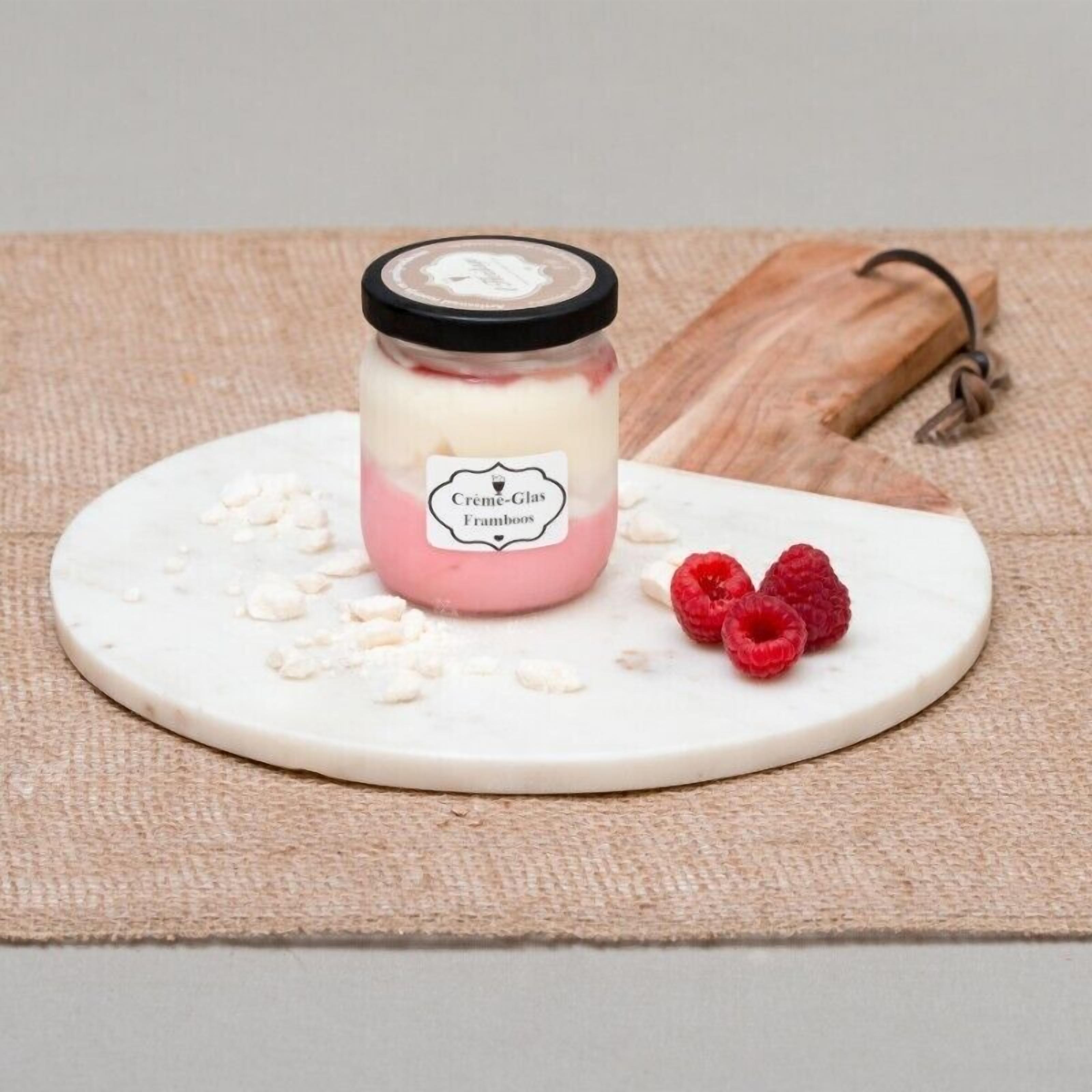 Un pot de Crème-Glas Framboos posé sur une surface en marbre blanc, avec quelques noix et deux framboises éparpillées autour.