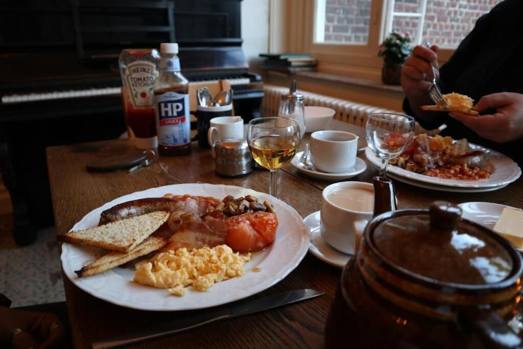A breakfast setting with plates of eggs, bacon, toast, and tomatoes, along with condiments and a coffee cup.