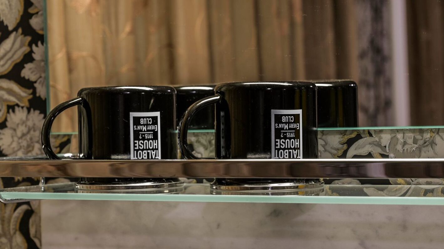 Trois tasses noires, chacune portant une étiquette, sont posées sur une étagère en verre.