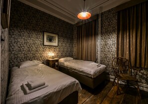 A room with two beds, a wooden chair, and a wall-mounted picture.
