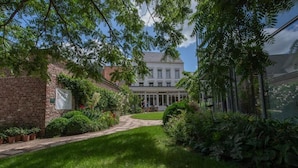 En innergård med en byggnad i tegel, en vit byggnad med en balkong och frodig grönska.