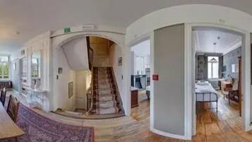 Vue panoramique d’un vaste espace de vie comprenant une grande table à manger en bois, un escalier et un coin cuisine.