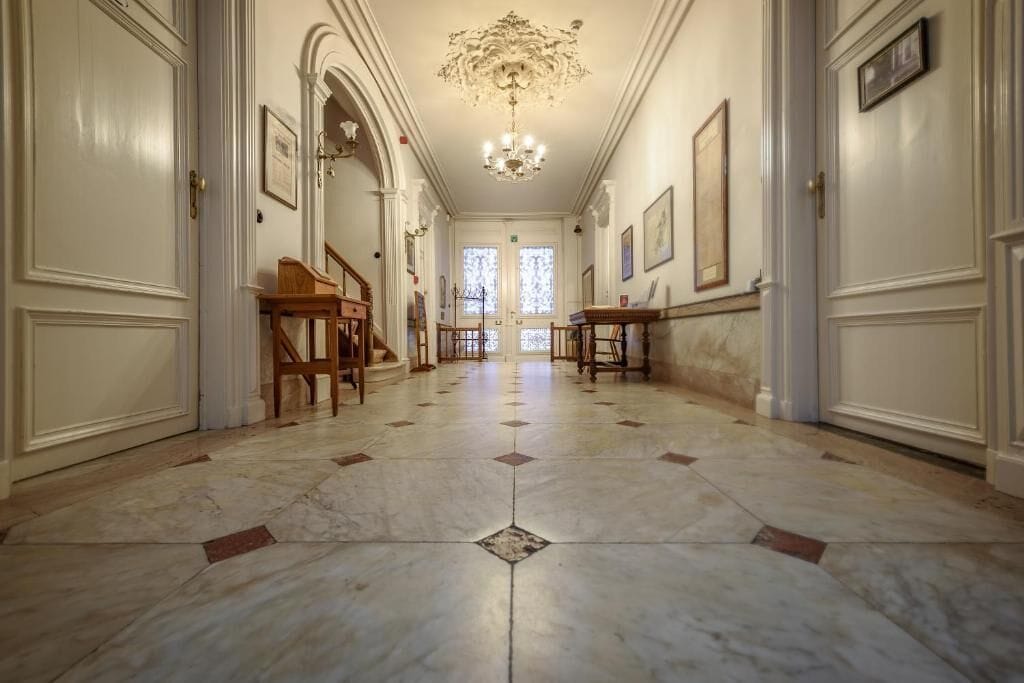 A hallway with marble flooring, wooden furniture, and framed artwork on the walls.