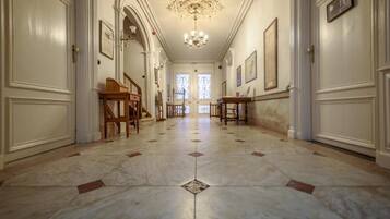 A hallway with marble flooring, wooden furniture, and framed artwork on the walls.