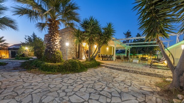 Un cortile lastricato in pietra con un edificio in pietra, palme e zona salotto all'aperto.