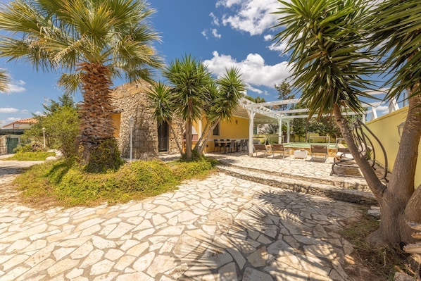A stone-paved courtyard with palm trees, a pergola, and outdoor seating.