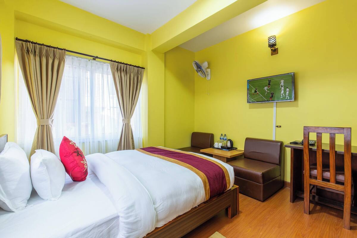 A hotel room with a bed, a desk, a chair, a TV, and curtains.