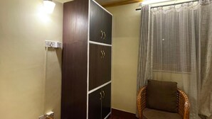 A room with a dark wooden wardrobe, a wicker chair, a glass table, and a window with curtains. - Deepjyoti Inn & Homestay (Kathmandu)
