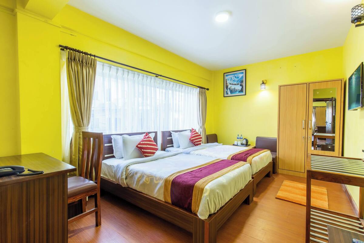 A hotel room with two beds, a desk, a wardrobe, and a television.