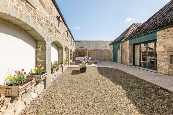 A courtyard with stone buildings, a gravel path, and outdoor seating. - Beautiful 5 bedroom Steading Conversion in Highland Perthshire (Pet Friendly) (Aberfeldy)