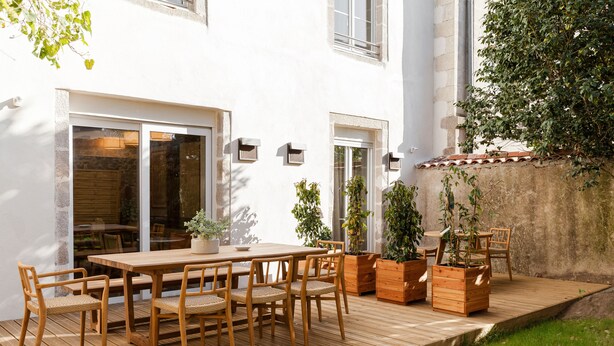 Une terrasse en bois avec une table et des chaises, entourée de plantes en pot.
