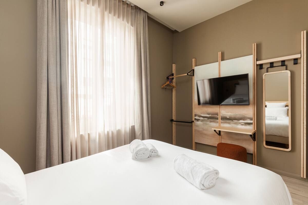 A hotel room with a bed, a TV, a mirror, and a wardrobe.