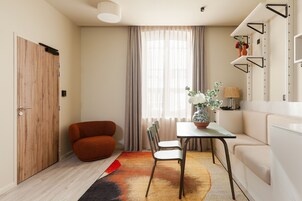 A compact living space with a wooden door, a red armchair, a dining table with chairs, a potted plant, and a white sofa.