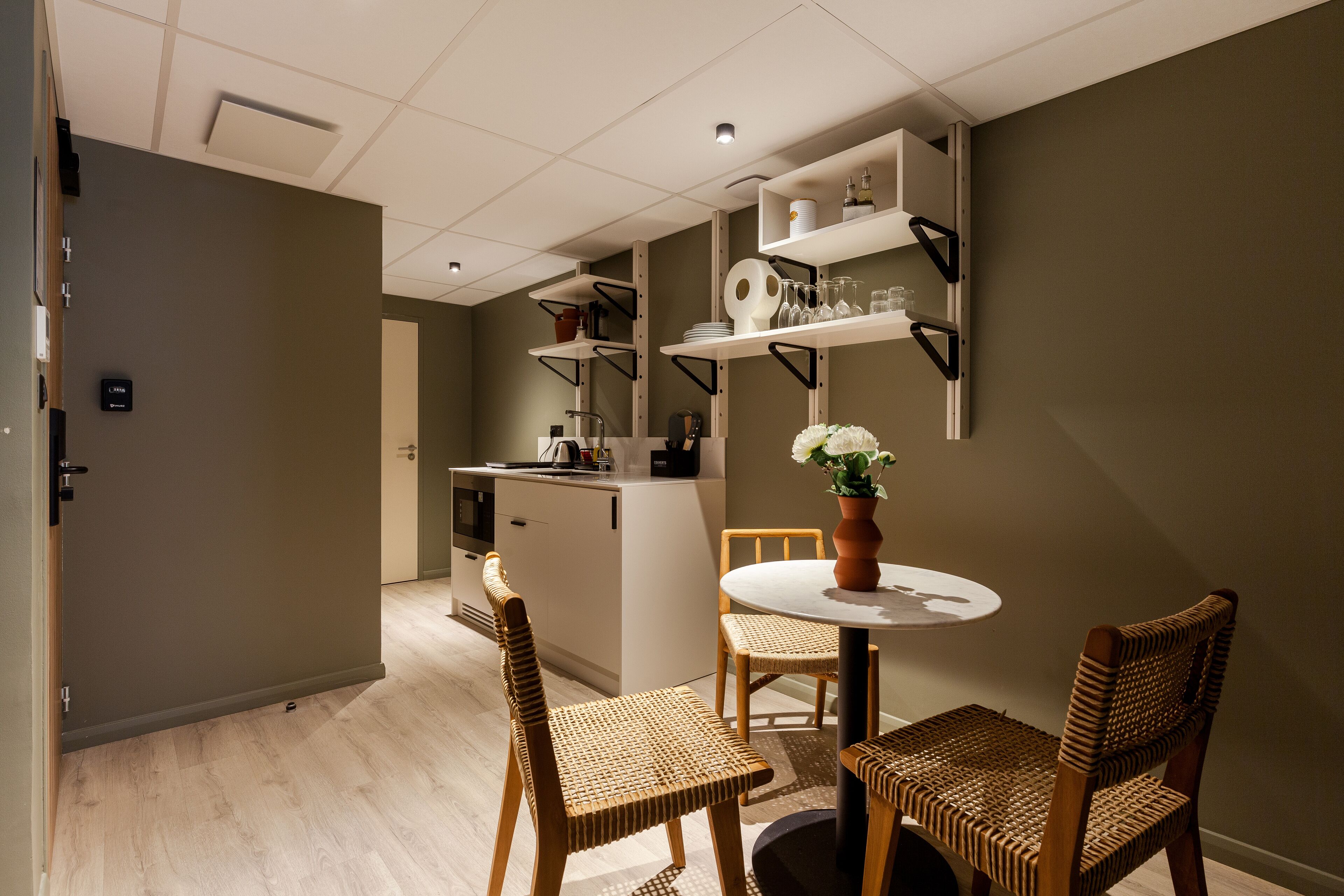 A modern kitchen with built-in appliances, a dining area with wicker chairs, and a small island with a vase of flowers.
