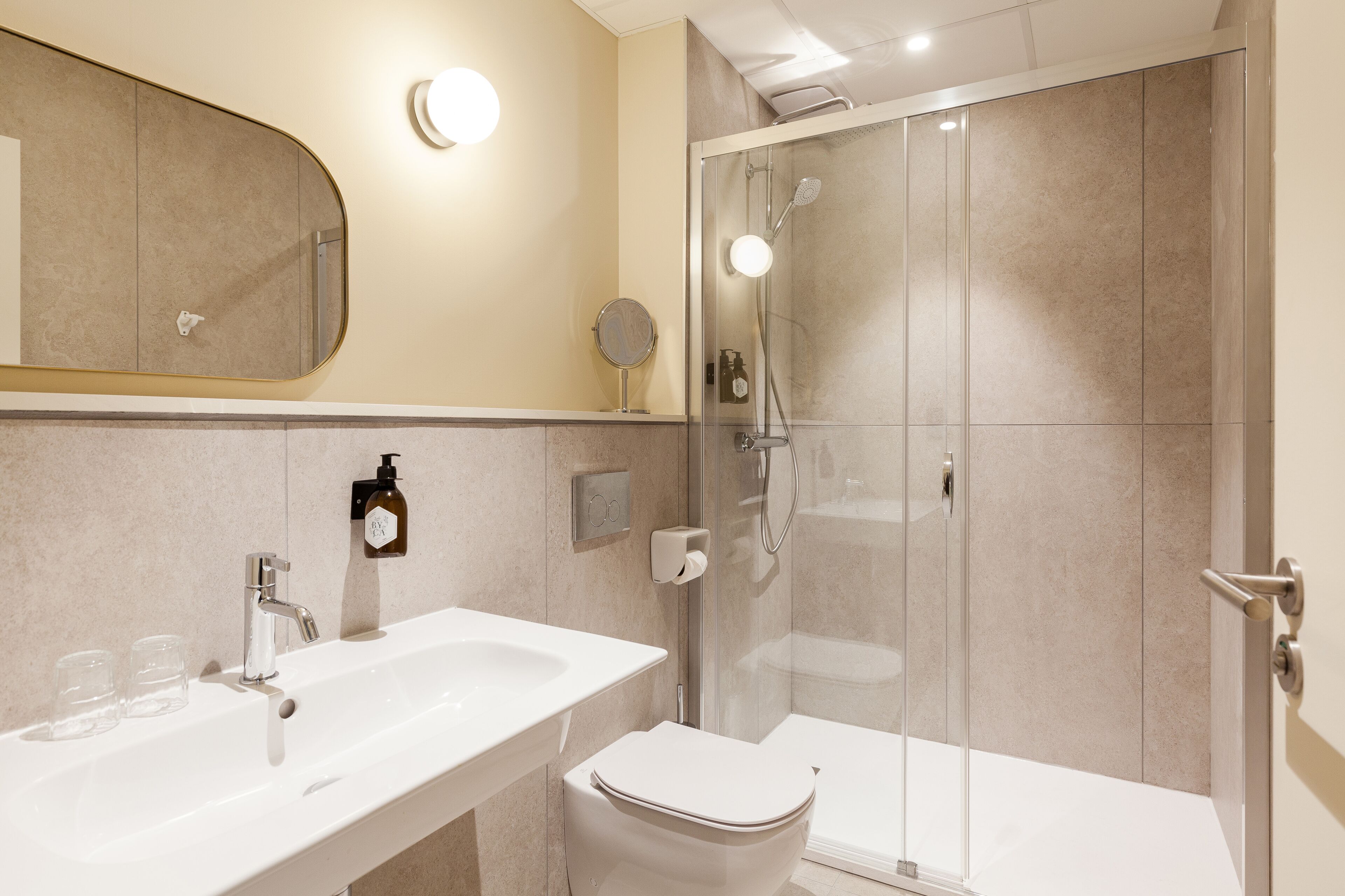 A modern bathroom with a white sink, mirror, and toilet, and a glass-enclosed shower area.
