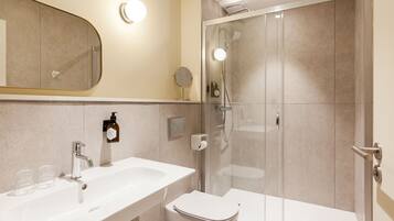 A modern bathroom with a white sink, mirror, and toilet, and a glass-enclosed shower area.
