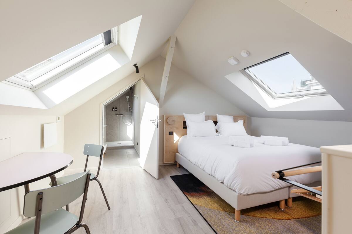 A bedroom with a skylight, a bed, a desk, and a chair.