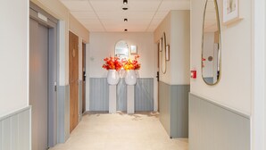 Un couloir d’hôtel avec un sol de couleur claire, des portes en bois et un arrangement floral au bout.