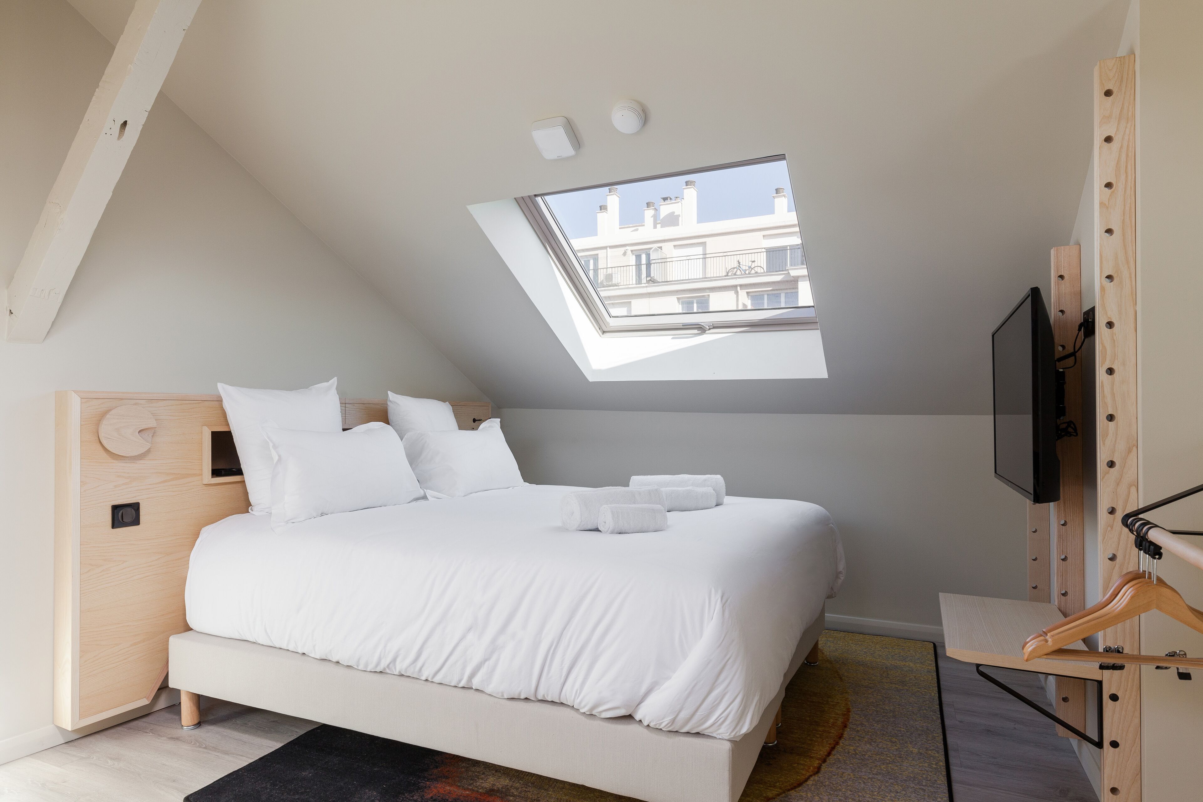 Een slaapkamer met dakraam, een bed, een televisie en een houten garderobe.