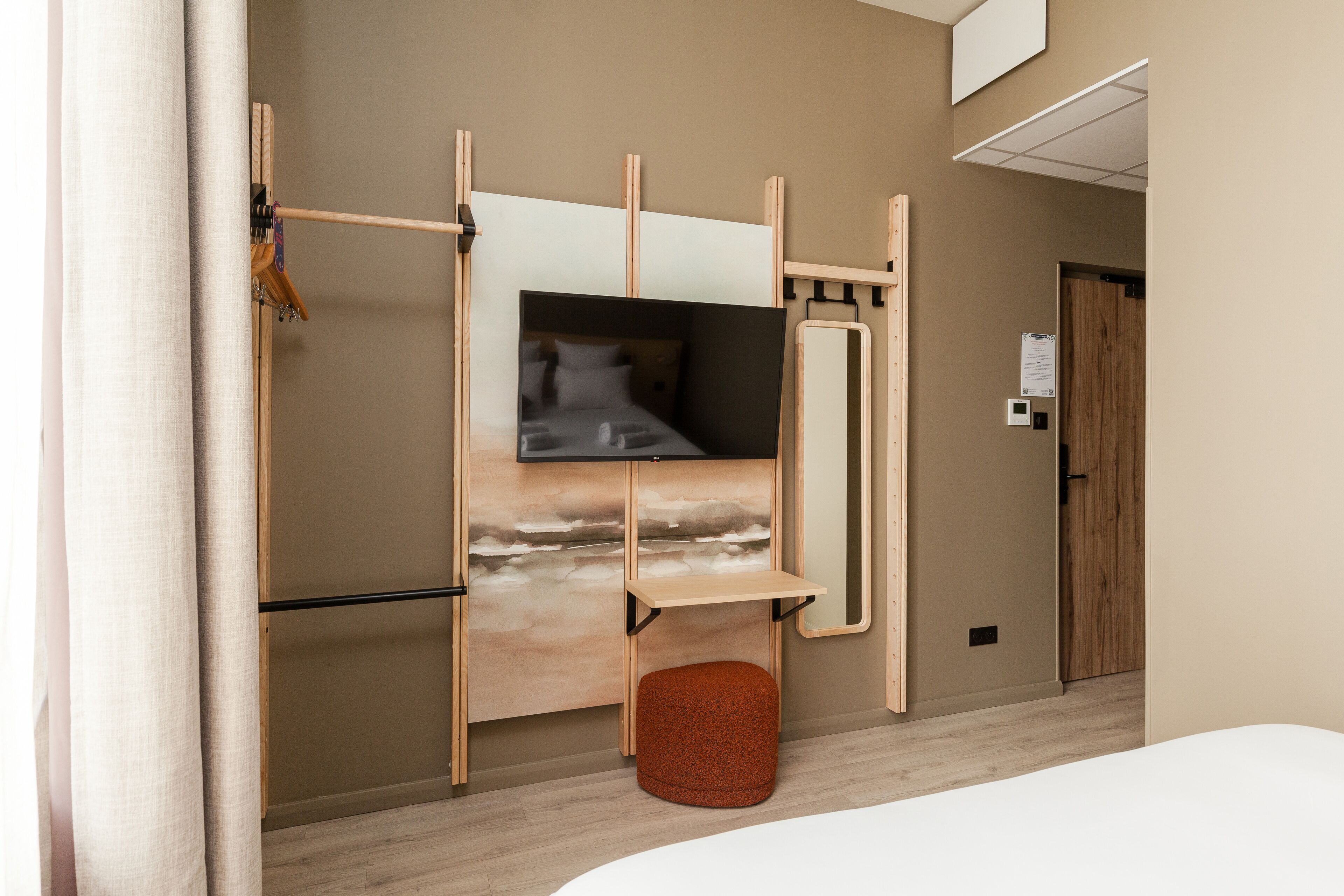 Ein modernes Hotelzimmer mit einem Bett, einem Fernseher, einem kleinen Hocker und einem Holzregal.