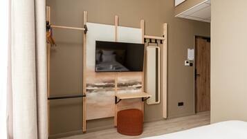 Ein modernes Hotelzimmer mit einem Bett, einem Fernseher, einem kleinen Hocker und einem Holzregal.