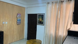 A room with a wooden door, a small round table, a curtain, and a framed picture on the wall. - Central Reservations Apartment (Accra)