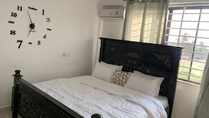 A bedroom with a bed, a wall clock, and a window with curtains. - Central Reservations Apartment (Accra)