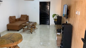 A living room with a sofa, coffee table, and TV stand. - Central Reservations Apartment (Accra)