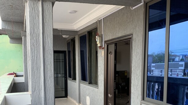 A corridor with tiled flooring, grey walls, and large windows offering views of the outside. - Central Reservations Apartment (Accra)