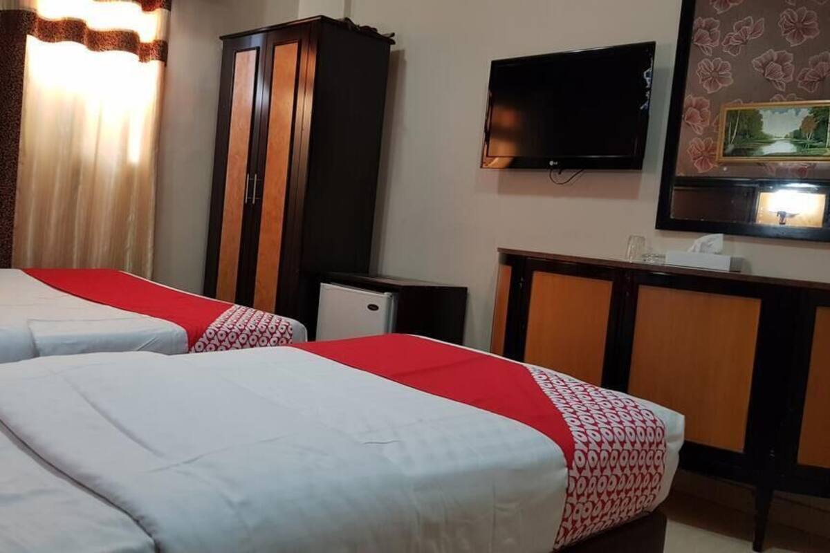 A hotel room with two beds, a TV, a small cabinet, and a framed picture on the wall.