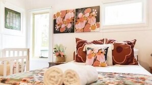 A neatly made bed with floral bedding, a small bedside table with a plant, and artwork above the bed.