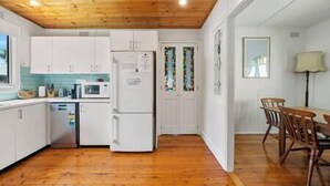 A kitchen with white cabinets, a microwave, and a refrigerator. There is a dining area with a table and chairs.