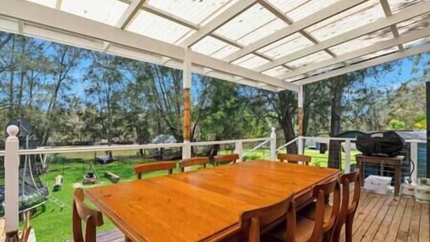 An outdoor wooden deck with a table and chairs, surrounded by a white pergola.