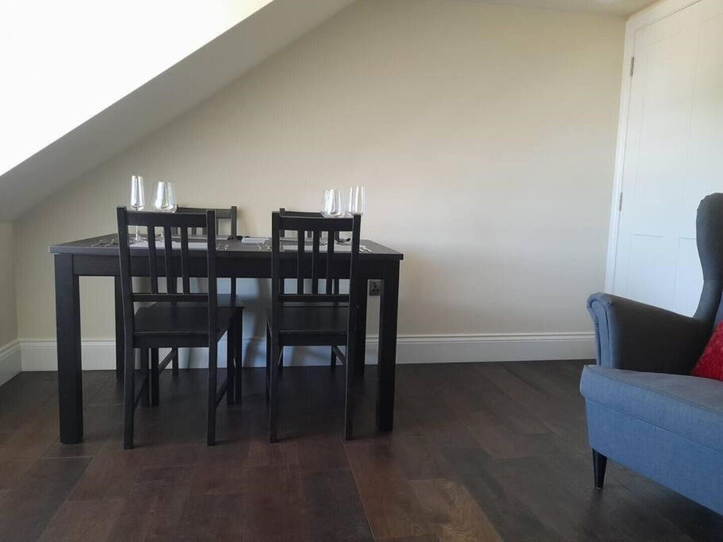 A dining area with a dark wooden table and chairs, a blue sofa, and a white door.