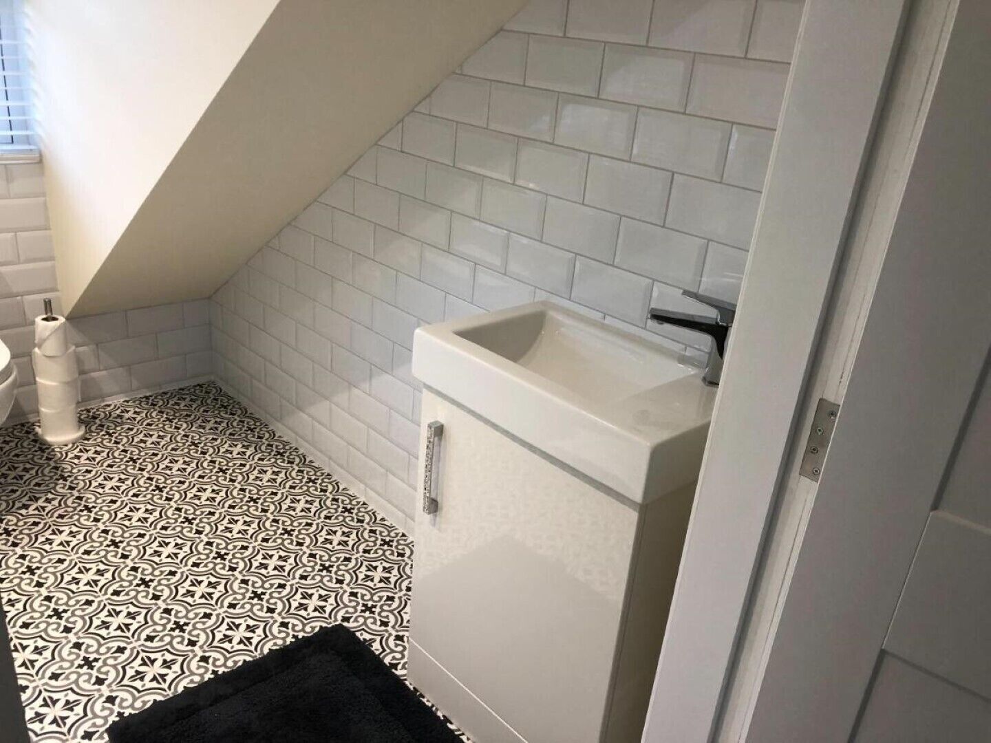Une salle de bain avec des carreaux blancs, un sol à motifs noir et blanc et un lavabo blanc.