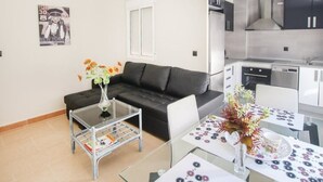 A modern living room with a black sofa, a glass coffee table, and a dining table with a floral centerpiece. - Apartamento de Vacaciones (Alacant)