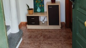 A hallway with a wooden cabinet, a painting, and a vase on a shelf.