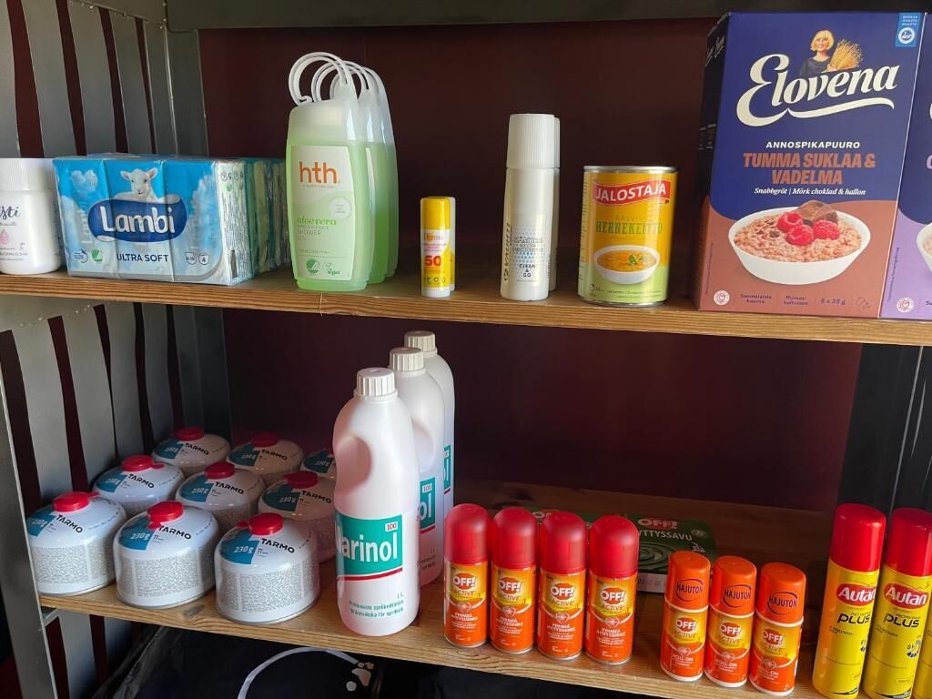 Des étagères remplies de divers articles ménagers, notamment des couches, des produits d’entretien et des produits alimentaires.