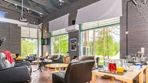 Amplia sala de estar con sofás de cuero, una mesa de madera con bebidas y grandes ventanales con vista a árboles.